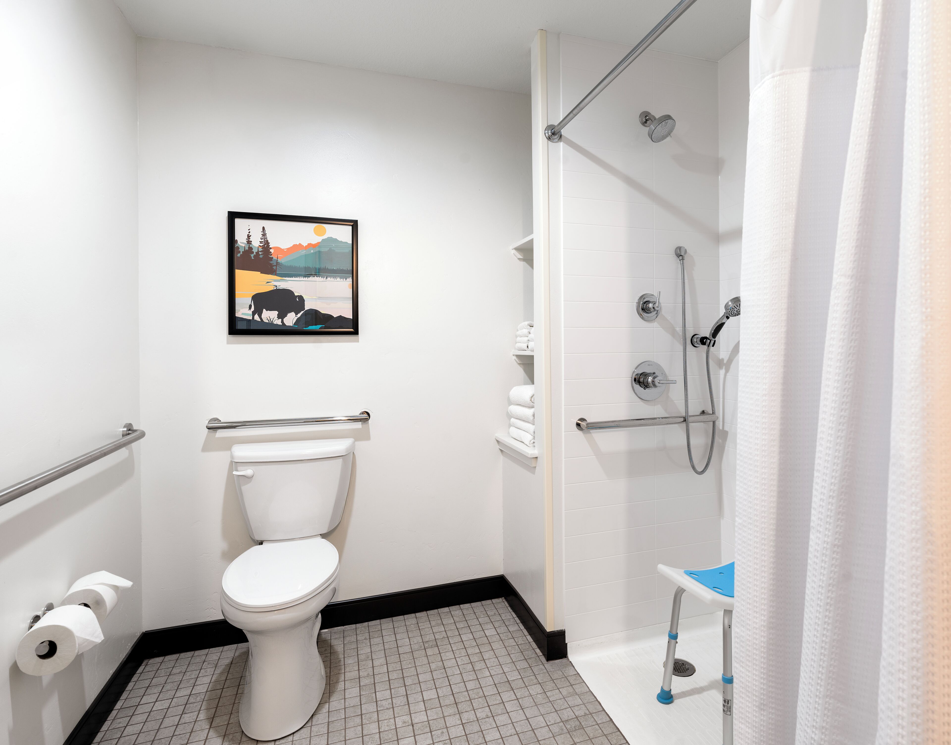 Et badeværelse med toilet, et billede i ramme på væggen og en bruseniche.