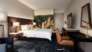 Una habitación de hotel con una cama, un escritorio, una silla, un televisor y un cuadro en la pared.