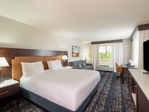 Habitación de hotel con una cama grande, un escritorio, una silla, un televisor y una ventana con cortinas.