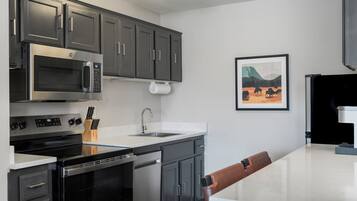 A modern kitchen with stainless steel appliances, a white countertop, and a dining area with a brown chair.