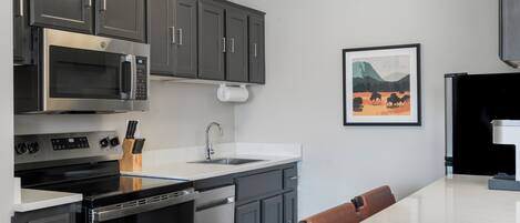 A modern kitchen with stainless steel appliances, a white countertop, and a dining area with a brown chair.