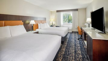 A hotel room with two beds, a desk, a television, and a window with curtains.
