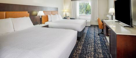 A hotel room with two beds, a desk, a television, and a window with curtains.