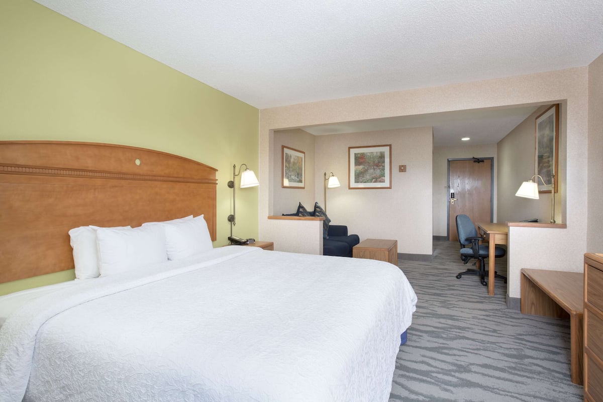 A hotel room with a large bed, a desk, a chair, and a desk lamp.