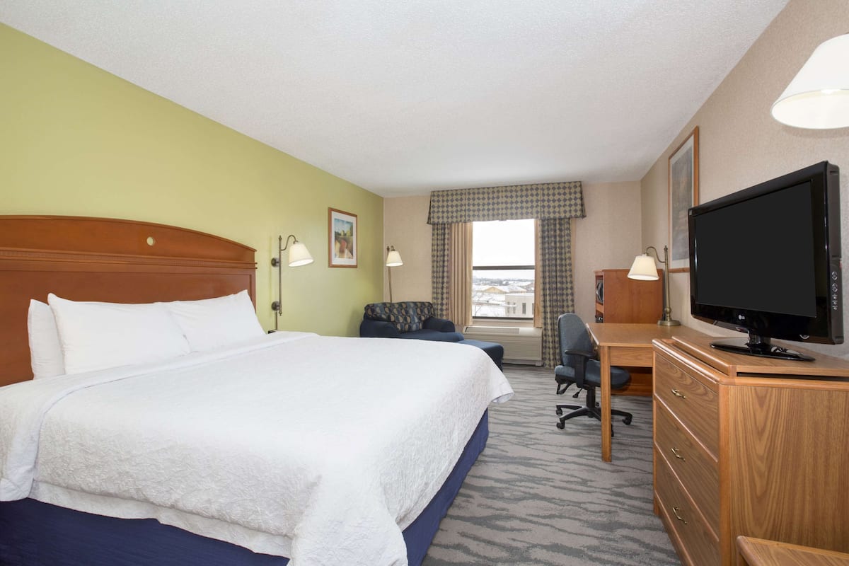 A hotel room with a large bed, a desk with a computer, a television, and a window with curtains.