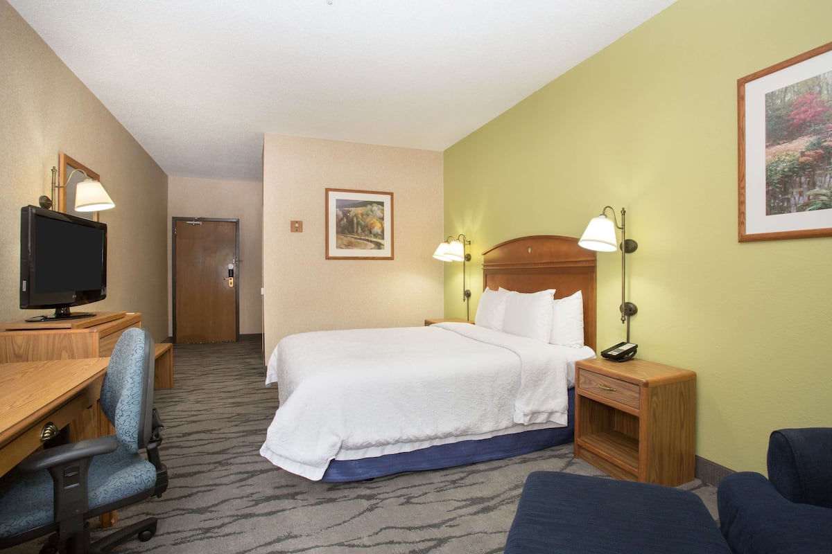 A hotel room with a bed, desk, chair, television, and two bedside lamps.