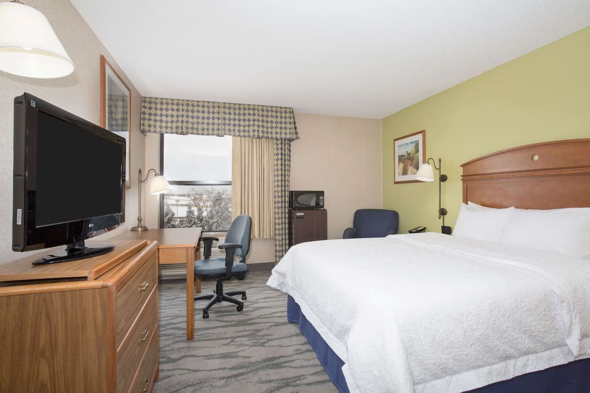 A hotel room with a bed, a desk with a computer, a television, and a window with curtains.