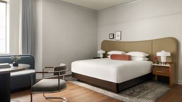 Una habitación de hotel moderna con una cama grande, una mesita de noche con lámparas, una pequeña mesa redonda con una silla y un sofá.