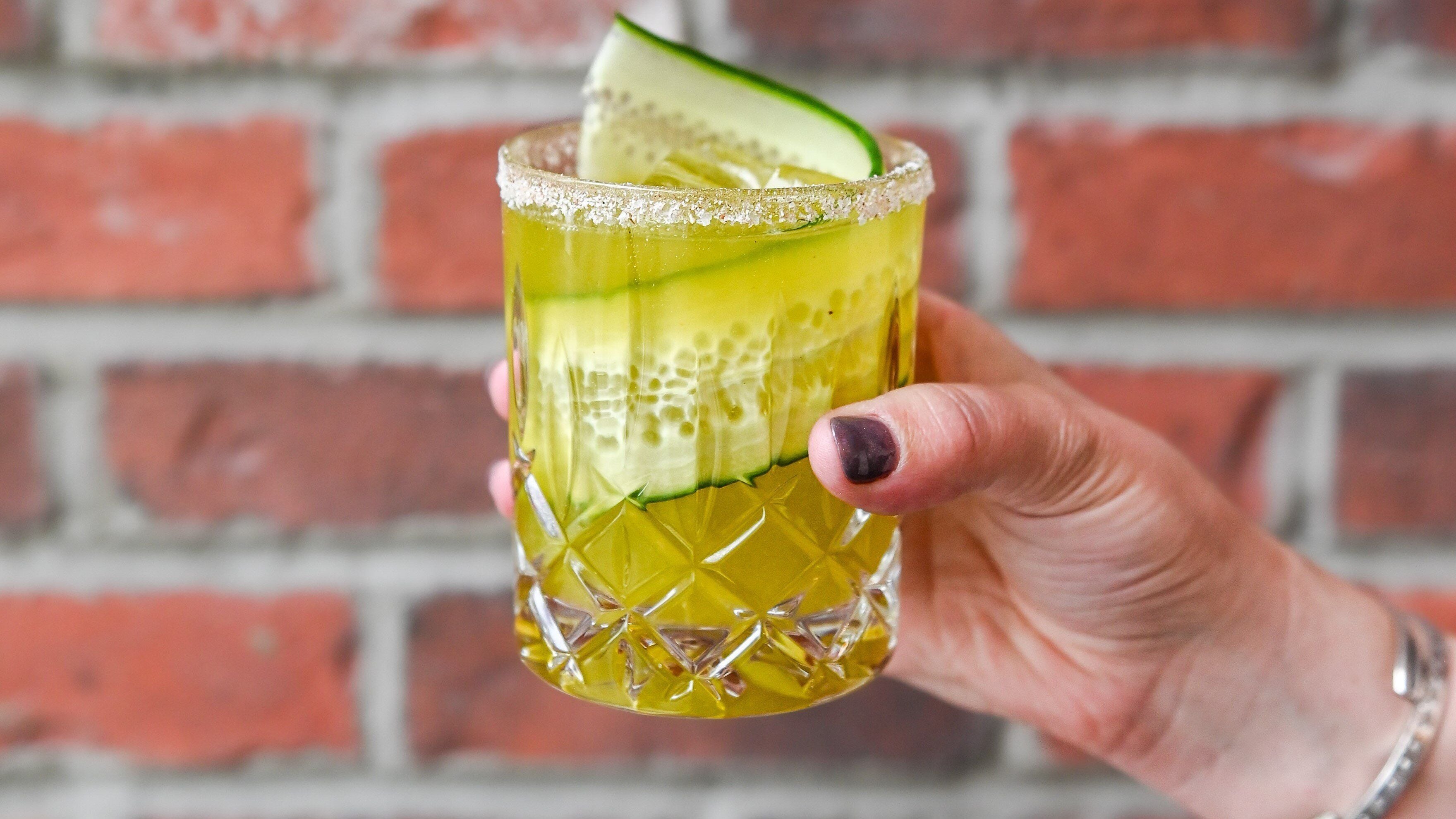 A hand holding a glass with a lime slice and a salted rim.