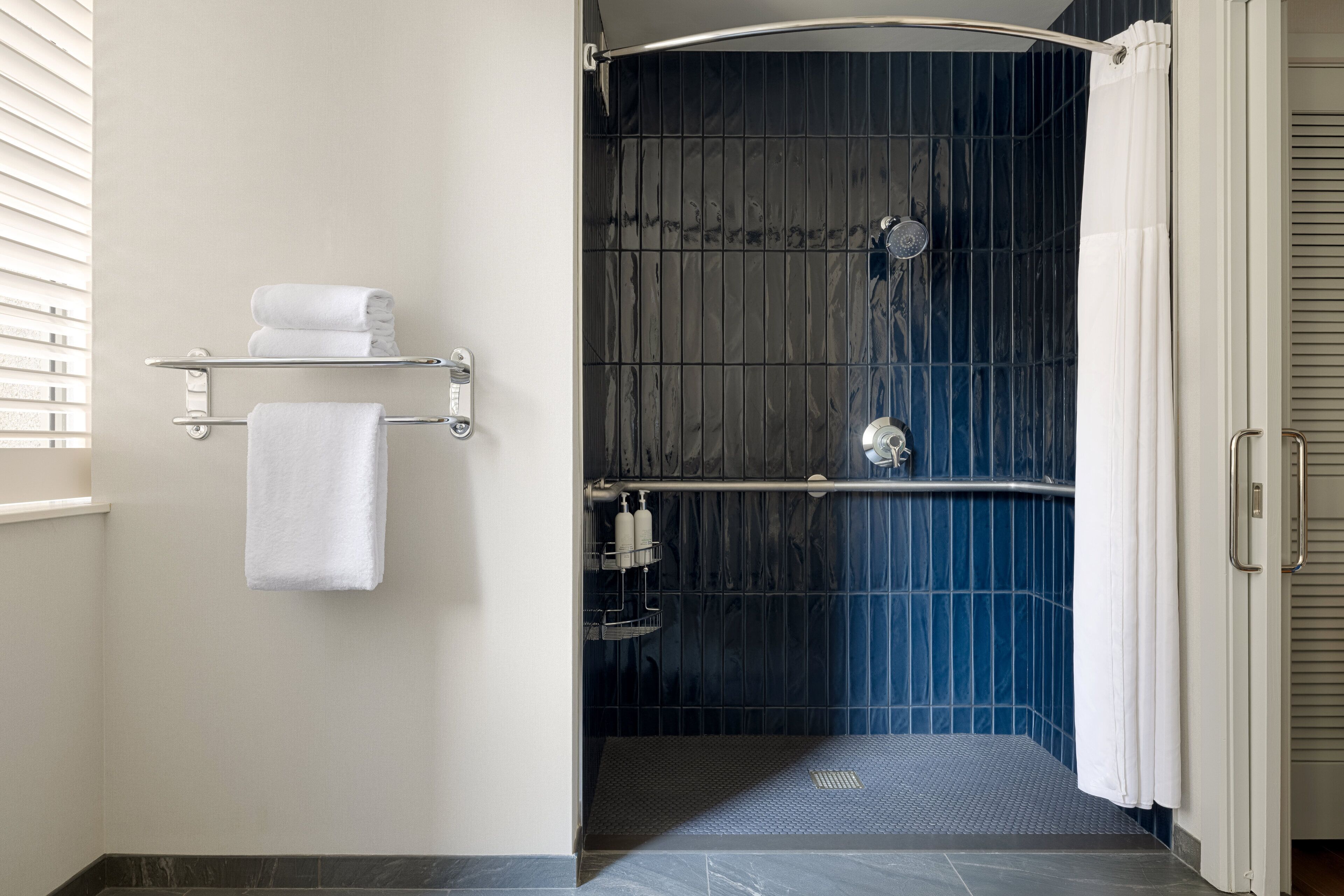 Un baño moderno con zona de ducha, un perchero y un estante con artículos de aseo.