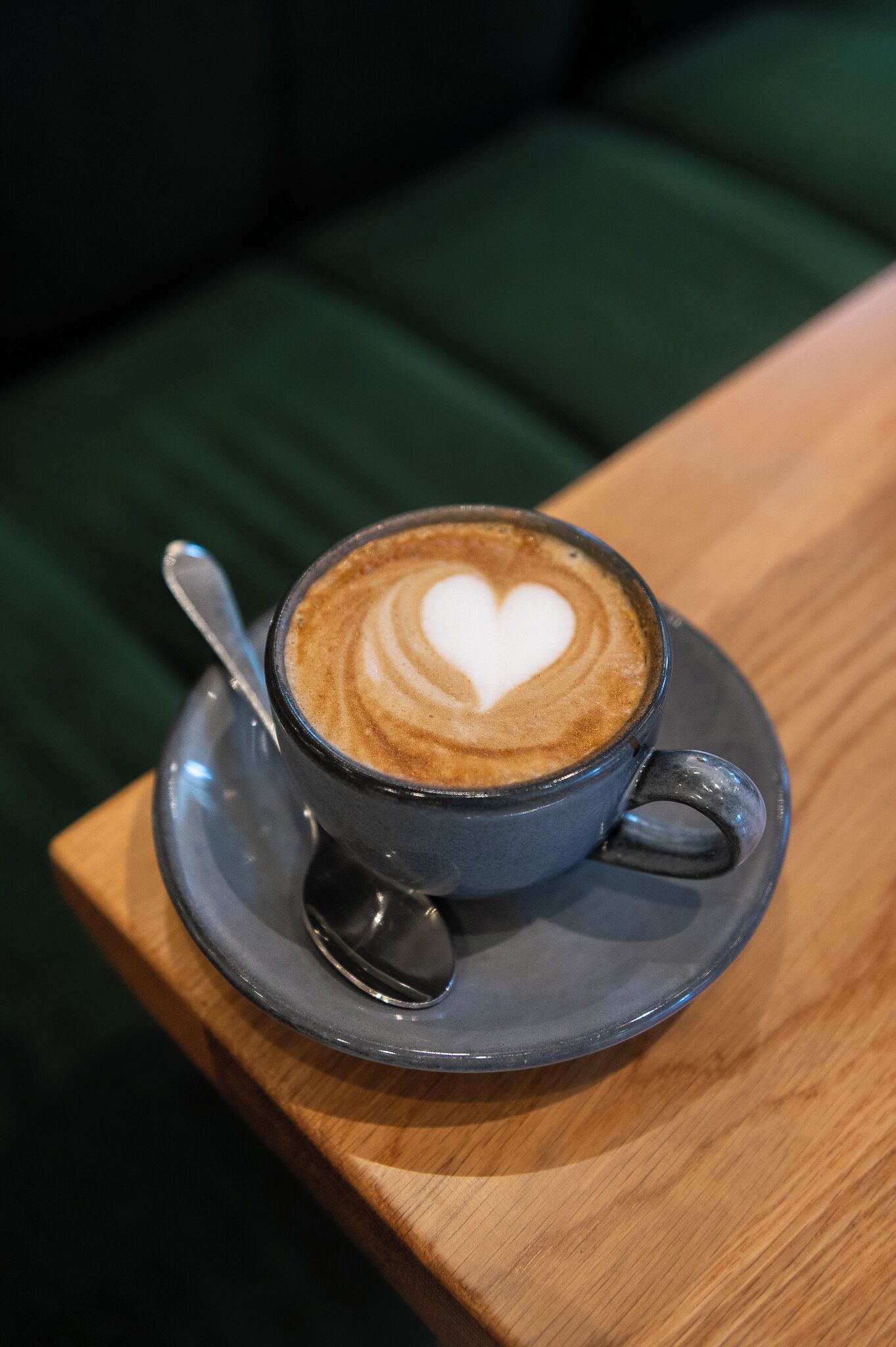 Una taza de café con un diseño de corazón en la espuma, sobre un plato posado en una mesa de madera.