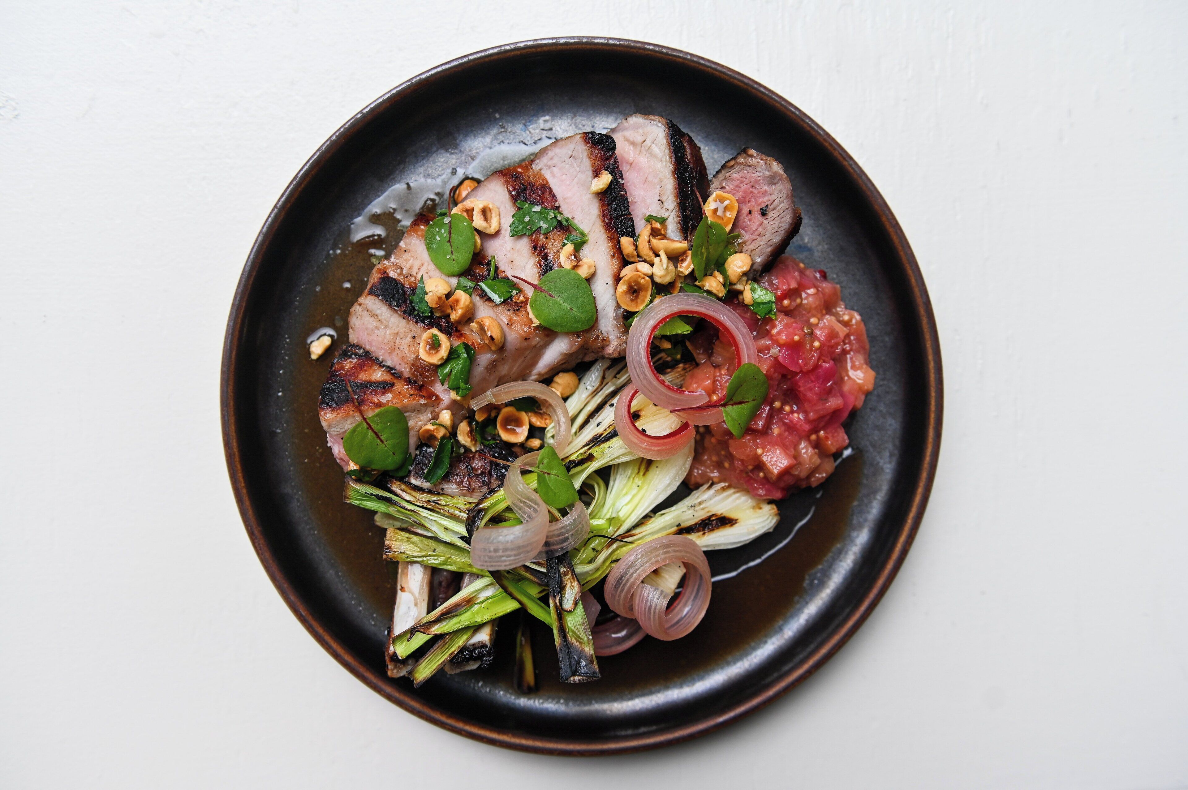 A plate of food with grilled meat, nuts, and vegetables.