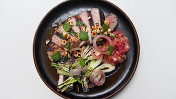 Un plato de comida con carne a la parrilla, frutos secos y verduras.
