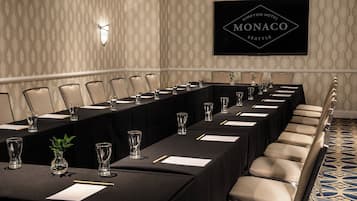 A conference room with a long table, chairs, and glassware, with a sign for 'Kimpton Hotel Monaco Seattle' on the wall.