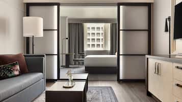 A modern hotel room with a sofa, a coffee table with a vase, a bed, a desk, and a television.