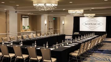 Ein Konferenzraum mit einem langen Tisch, Stühlen und einem Bildschirm, der 'Kimpton Hotel Monaco Seattle' anzeigt.