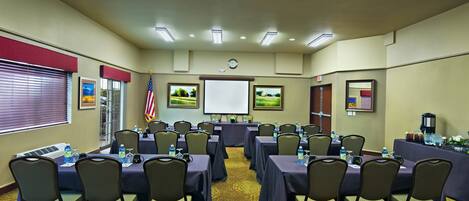 A conference room with multiple tables, chairs, and a projector screen.
