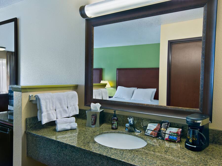 A hotel bathroom with a granite countertop, a sink, a mirror, and a coffee maker.