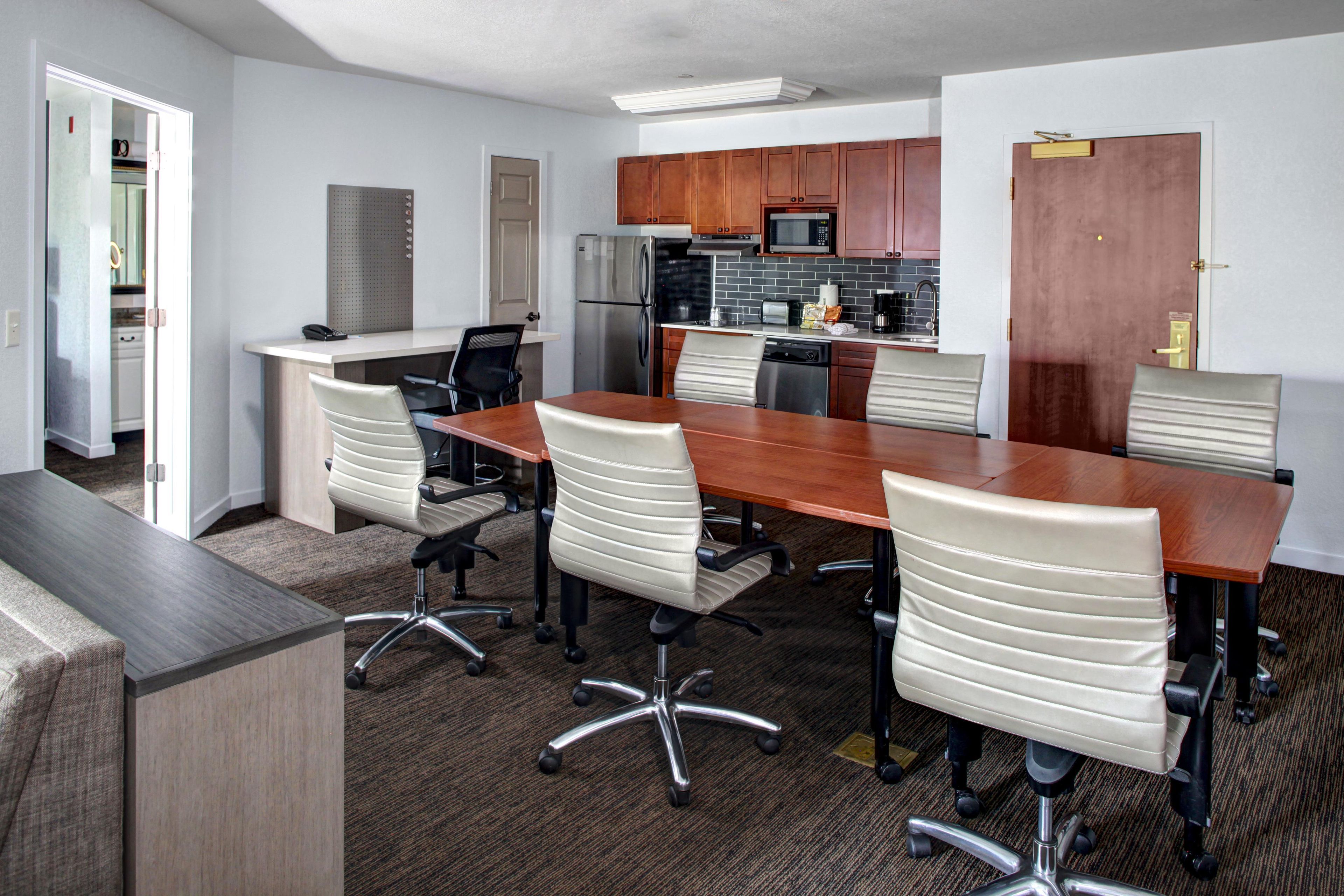 A conference room with a long table, four chairs, a refrigerator, a microwave, and a sink.