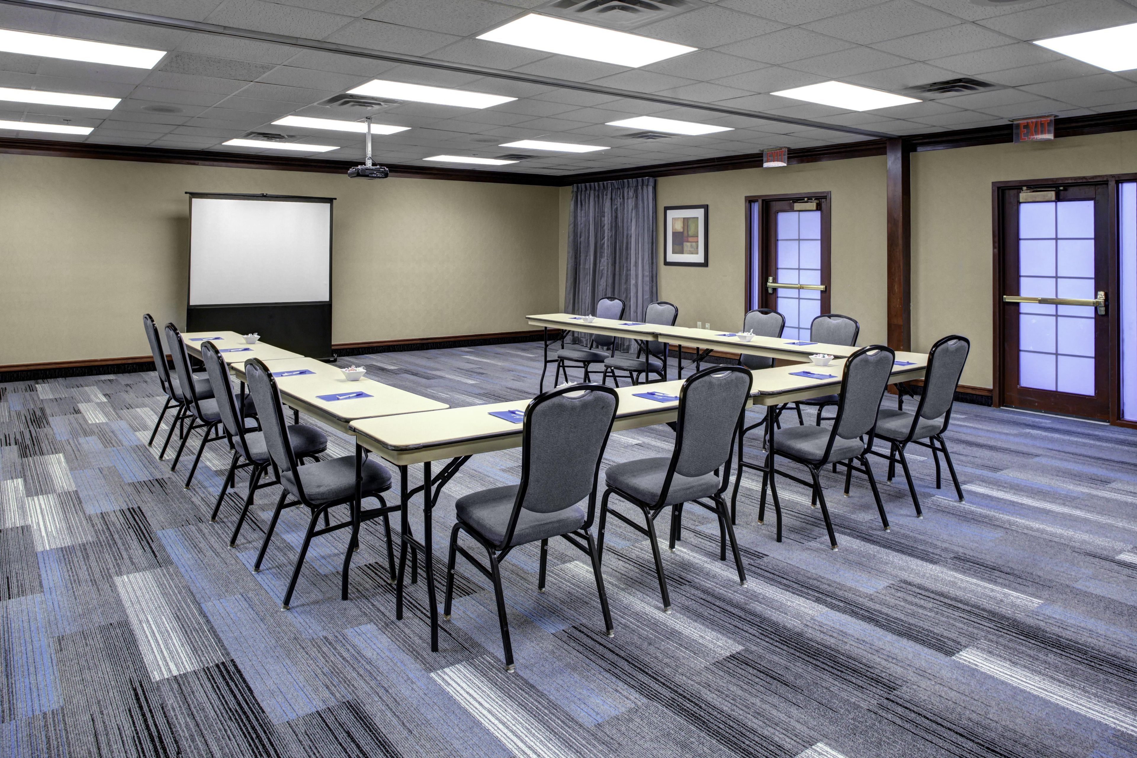 A conference room with a long table, chairs, a projector screen, and an exit door.