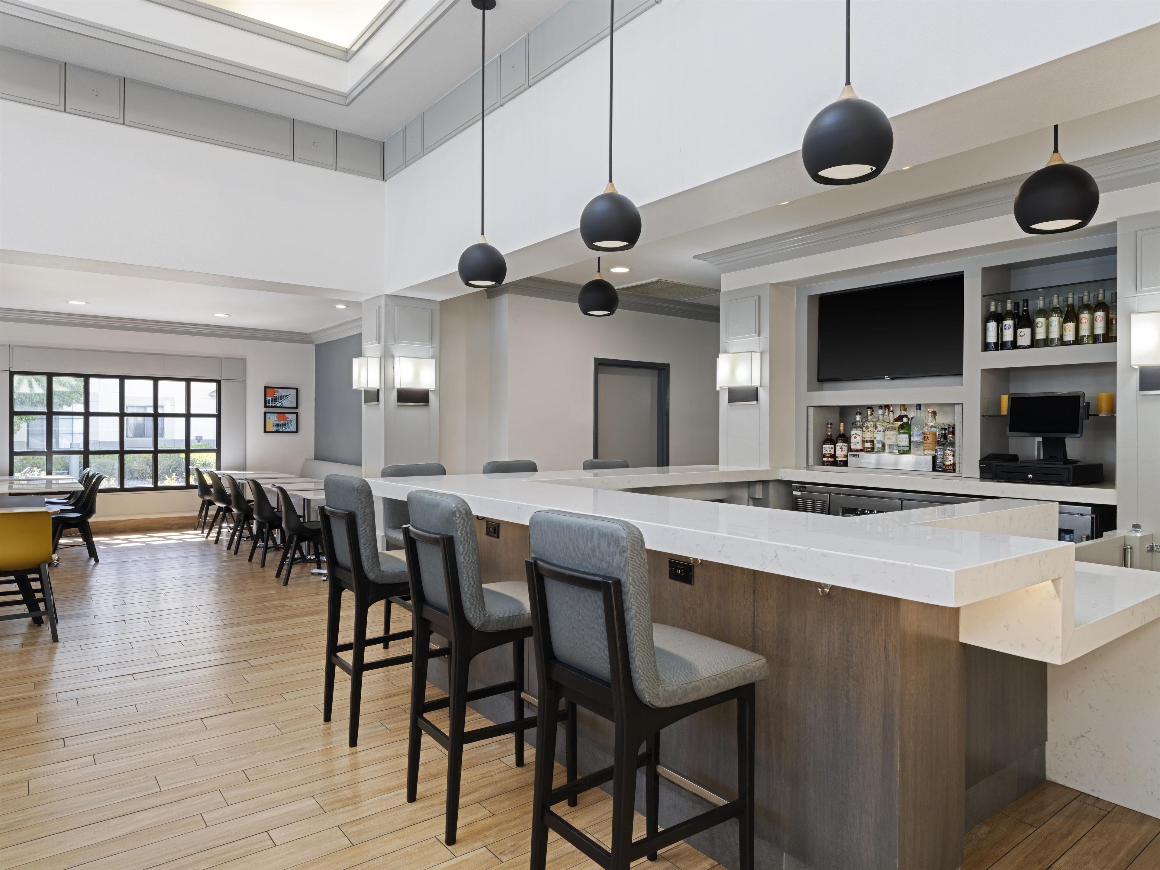 A modern bar area with a long counter, bar stools, pendant lighting, and a wine display.