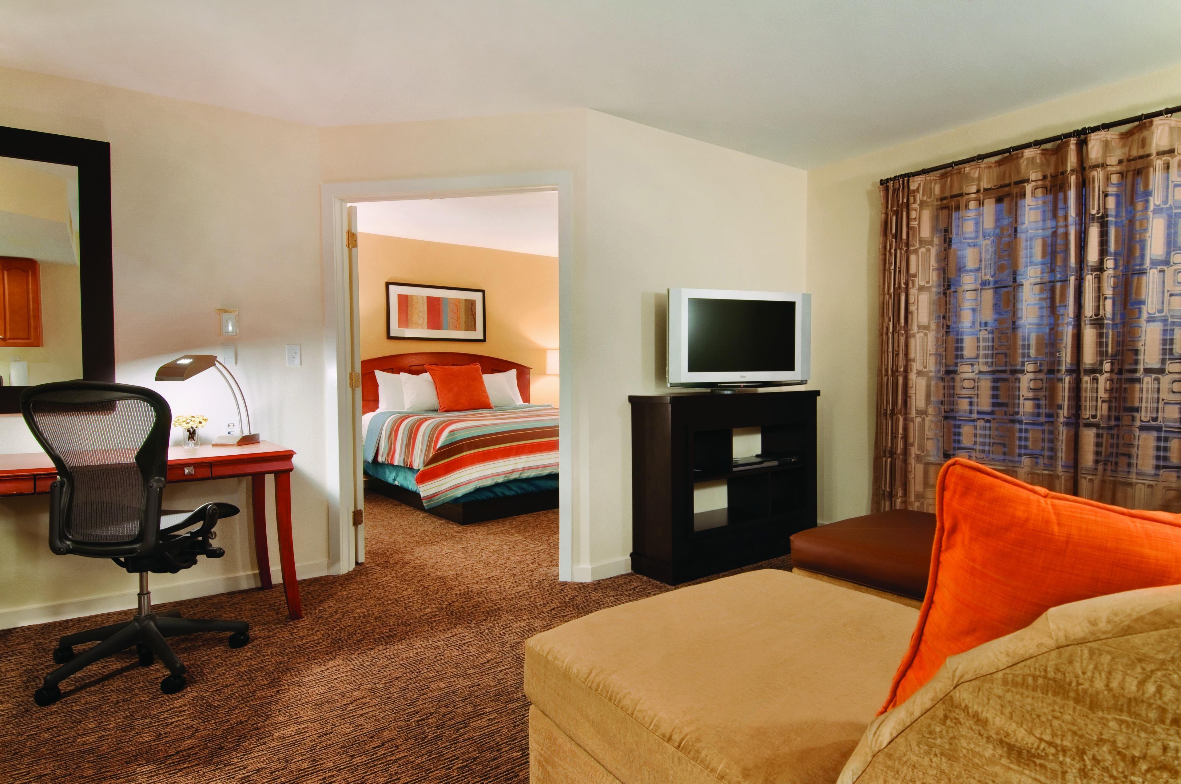 Una habitación de hotel con una cama, un escritorio con una silla, un televisor y un sofá.