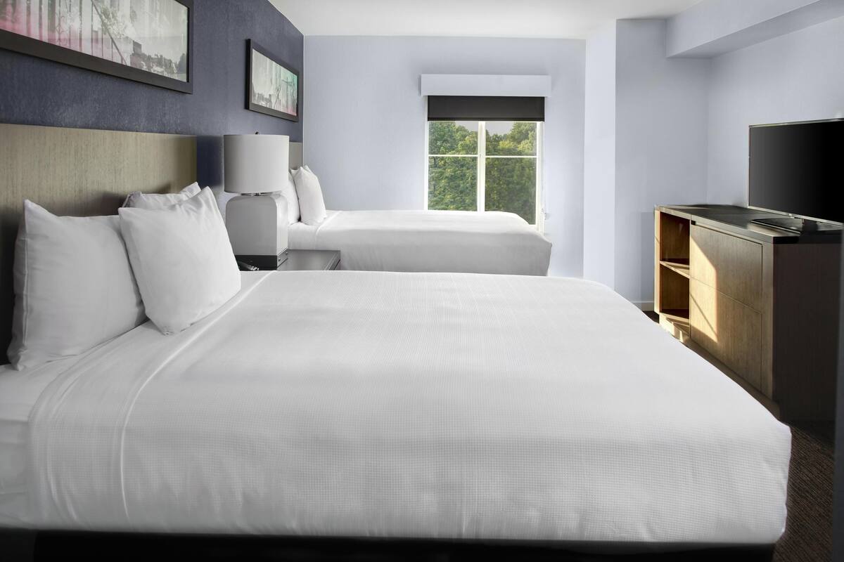 A hotel room with a large bed, a smaller bed, a TV, and a window with a view of trees.