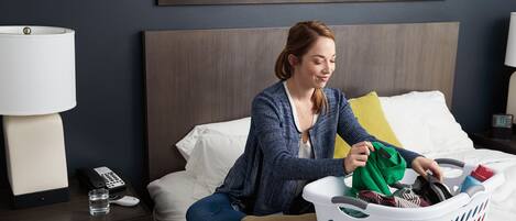 A hotel room with a bed, a nightstand with a lamp, a phone, and a laundry basket.