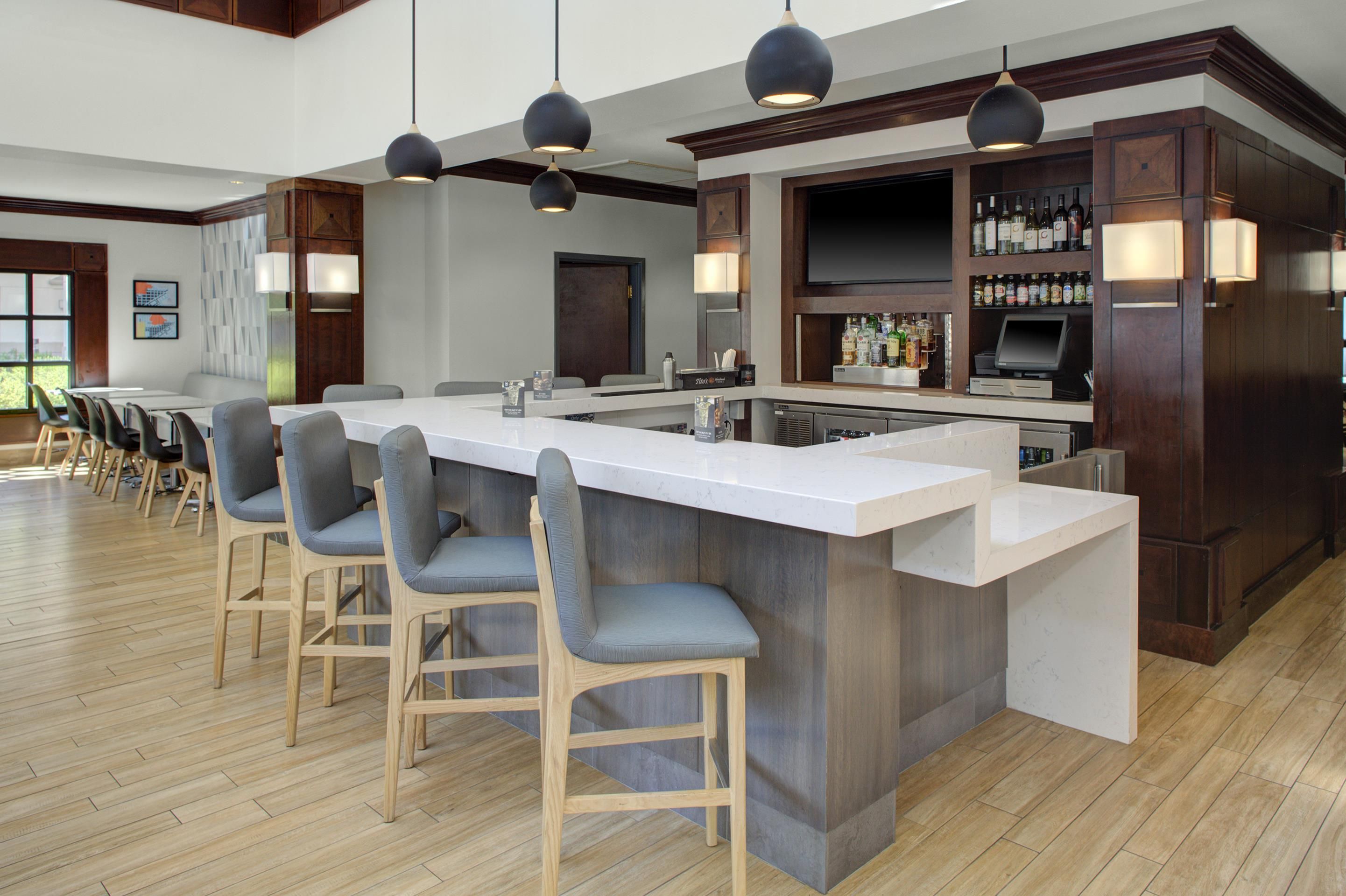 A bar area with a long counter, bar stools, and a selection of bottles.