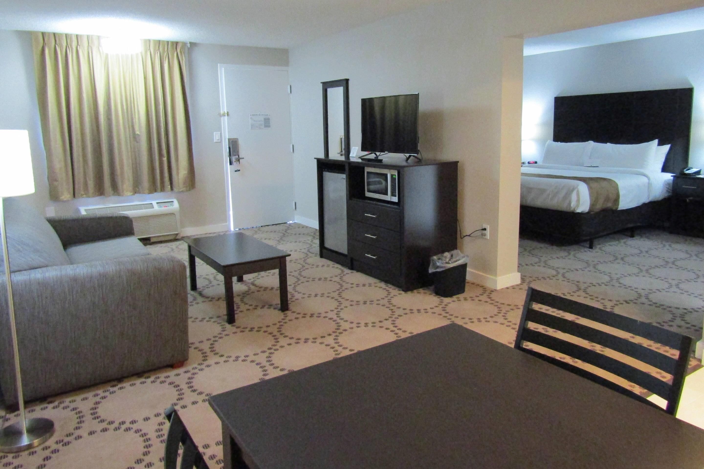 A hotel room with a bed, a desk, a dresser, a television, and a window with curtains.