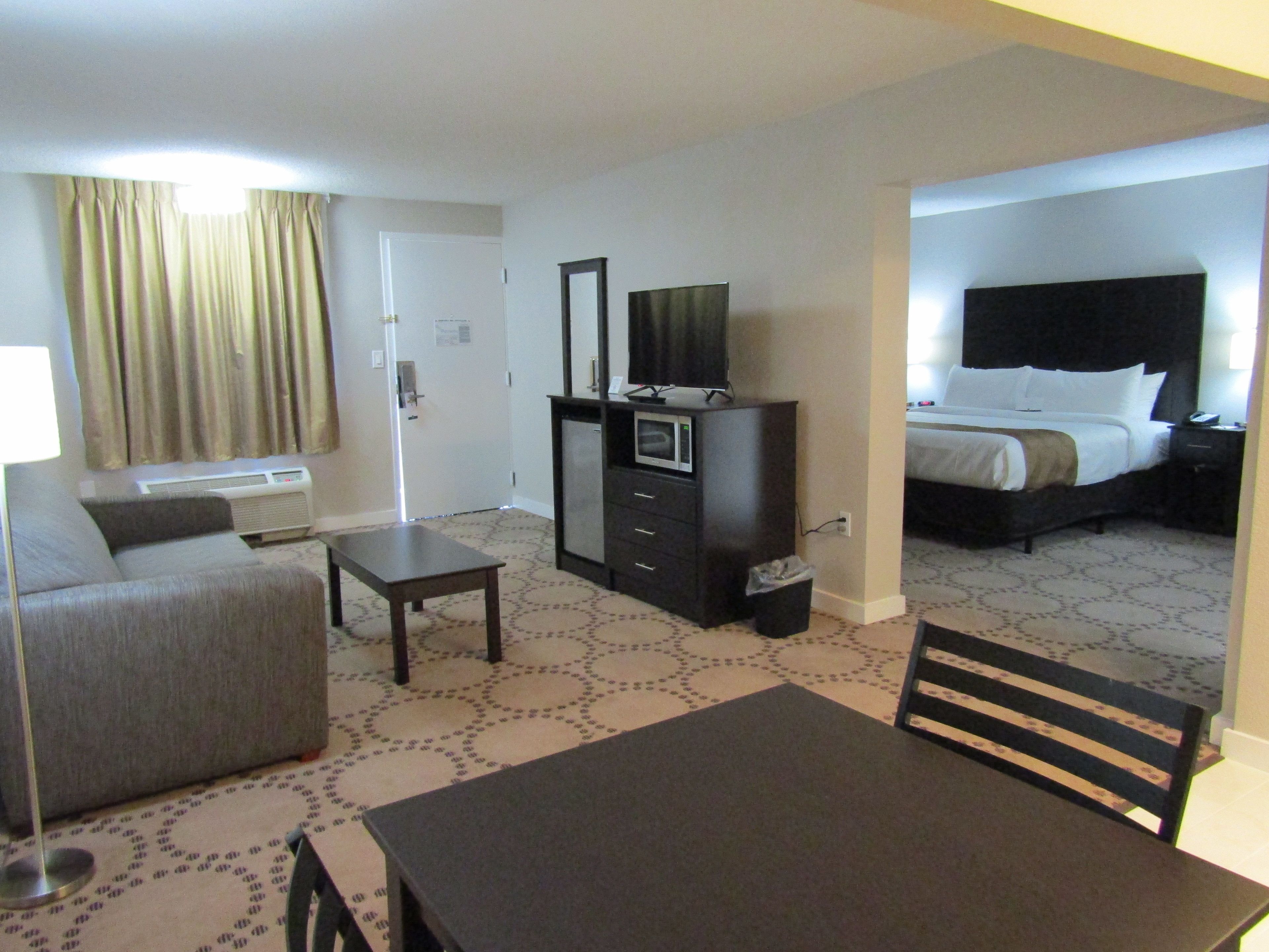 Una habitación de hotel con cama, escritorio, silla, televisor y una pequeña kitchenette.