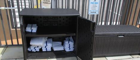 A portable storage unit with towels and a sign indicating 'Clean Towels' and 'Pool Rules'.