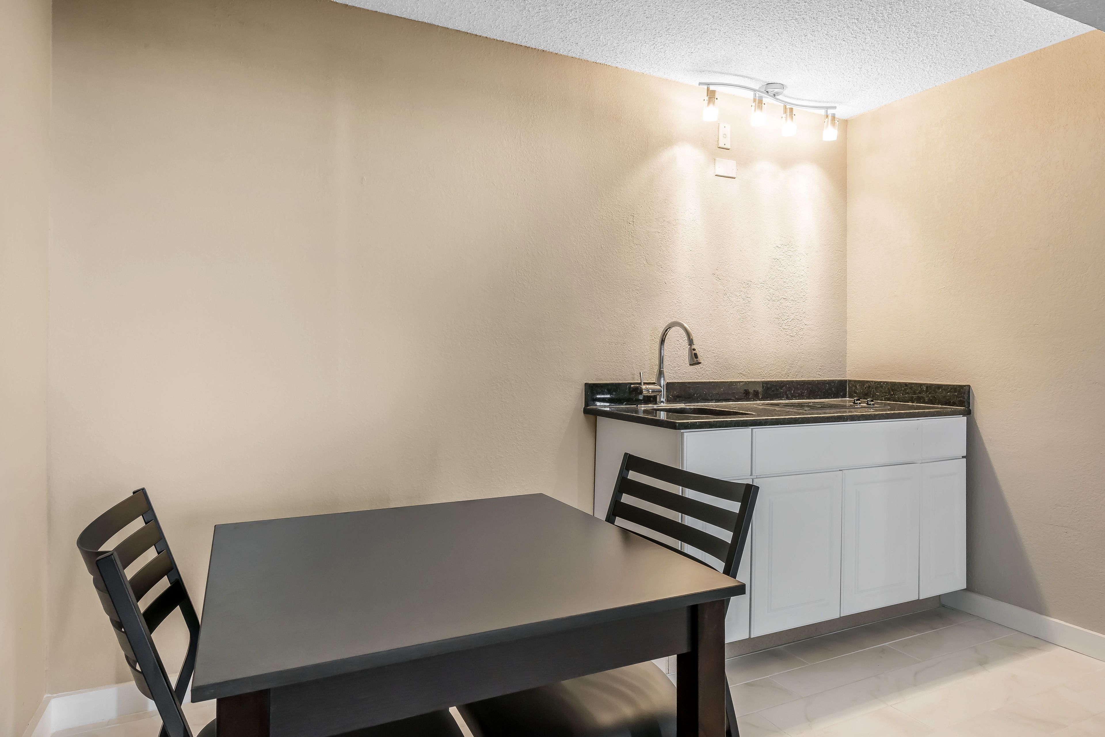 A compact kitchen with a dark countertop, white cabinets, and a single chair.