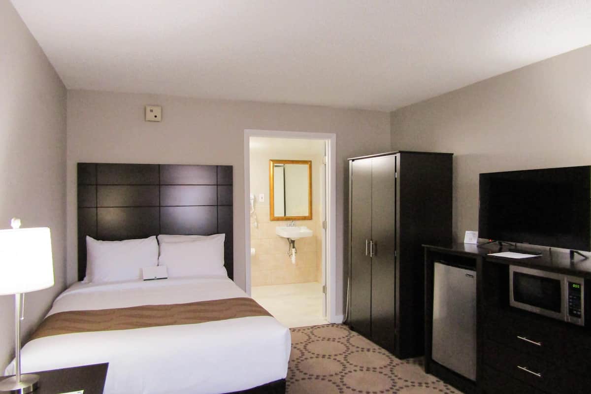 A hotel room with a bed, a desk with a lamp, a wardrobe, a television, and a bathroom visible through an open door.