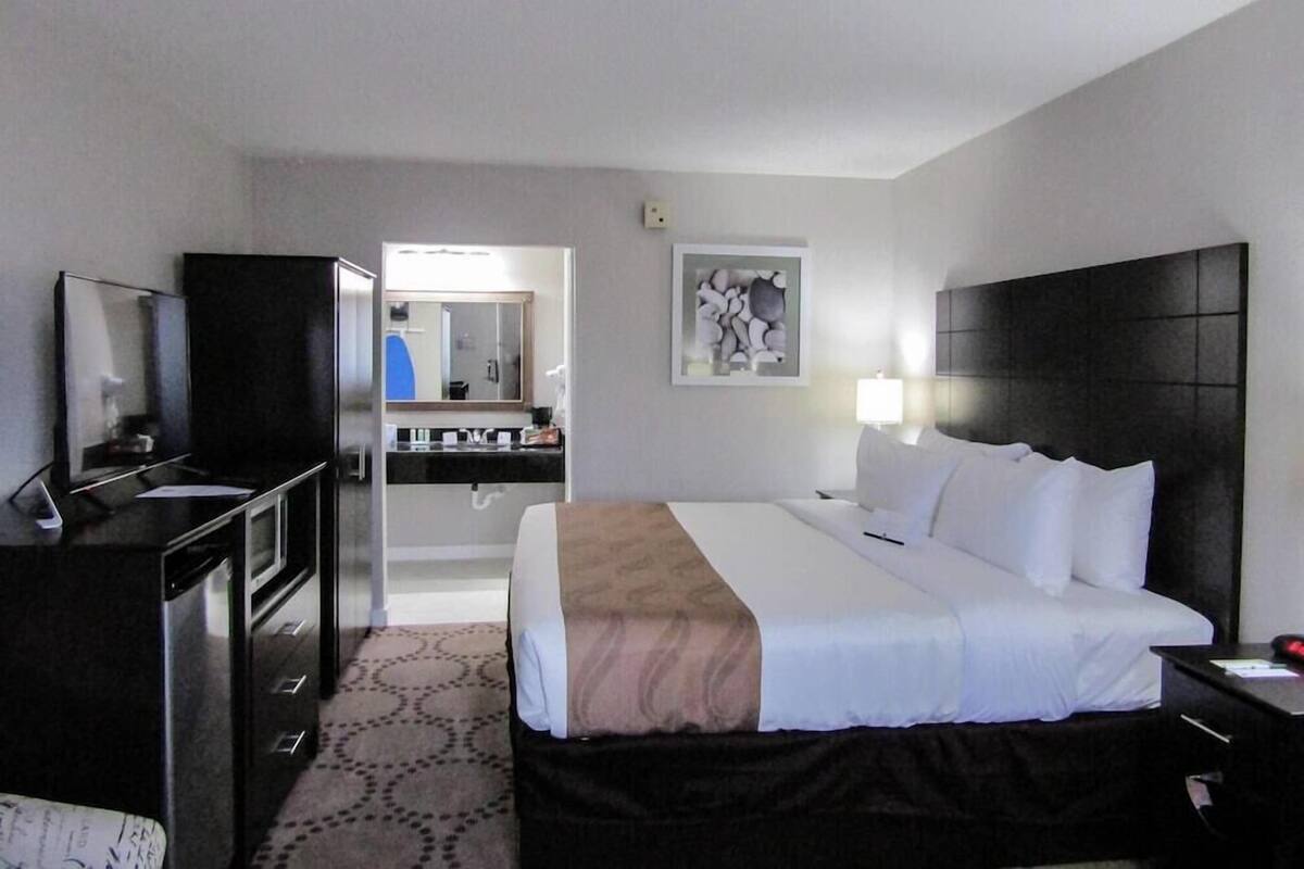 A hotel room with a bed, a desk, a television, a mirror, and a bathroom visible through an open door.
