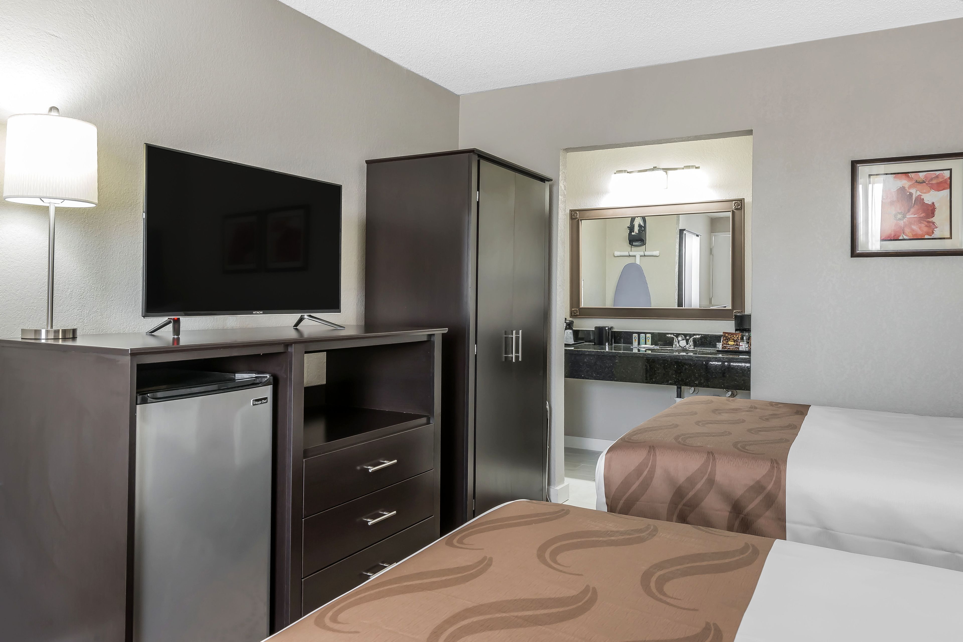 A hotel room with a bed, a television, a refrigerator, a cabinet, and a bathroom with a mirror.