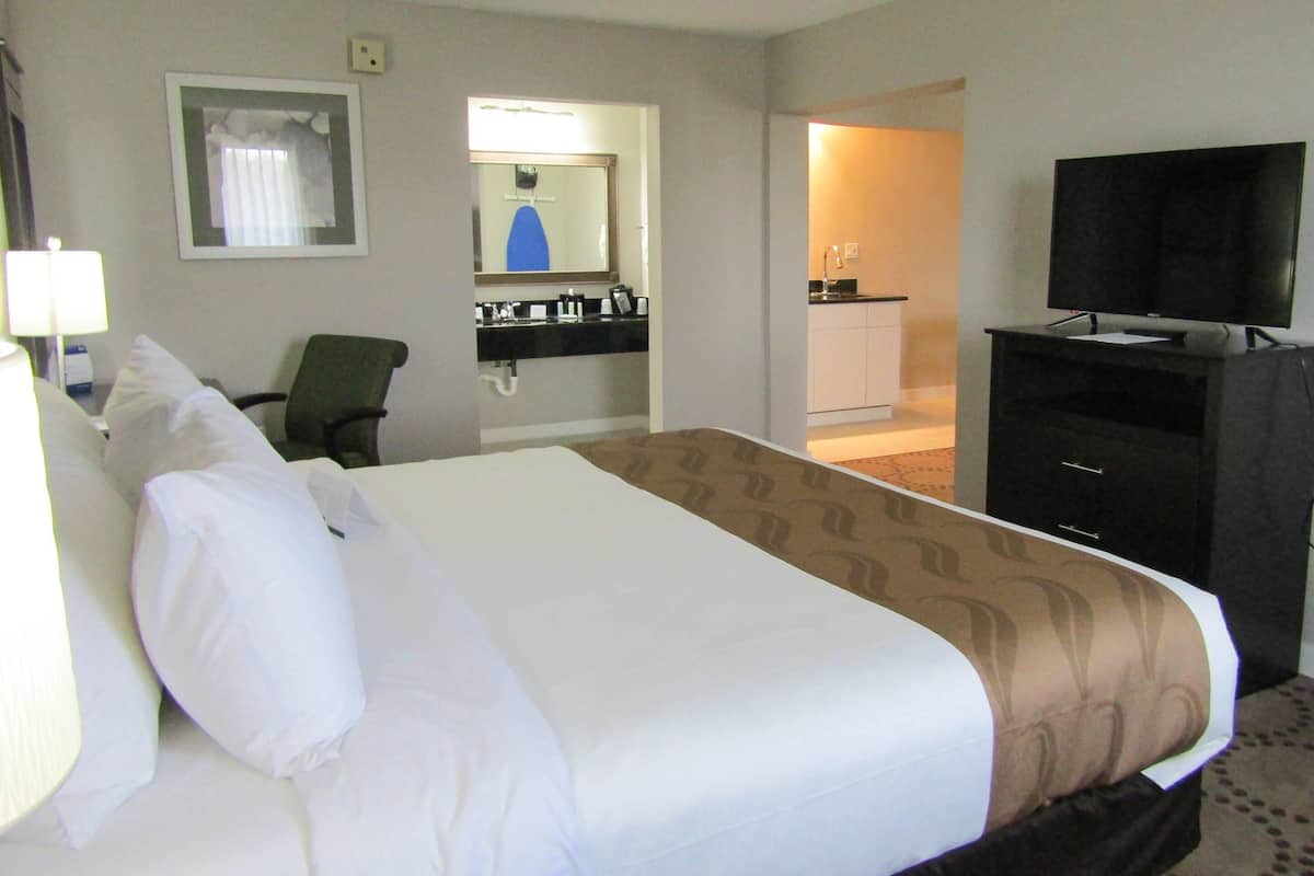 A hotel room with a bed, a desk, a chair, a TV, and a bathroom visible through an open door.