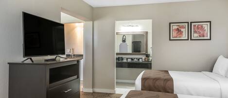 A hotel room with a TV, a dresser, two beds, a bathroom with a mirror, and two framed pictures on the wall.