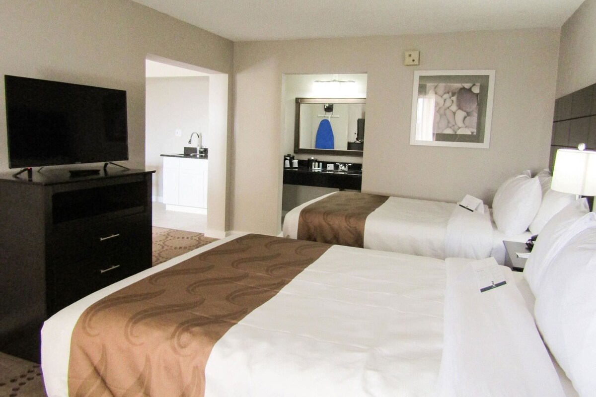 A hotel room with two beds, a TV, a desk, and a bathroom visible through an open door.