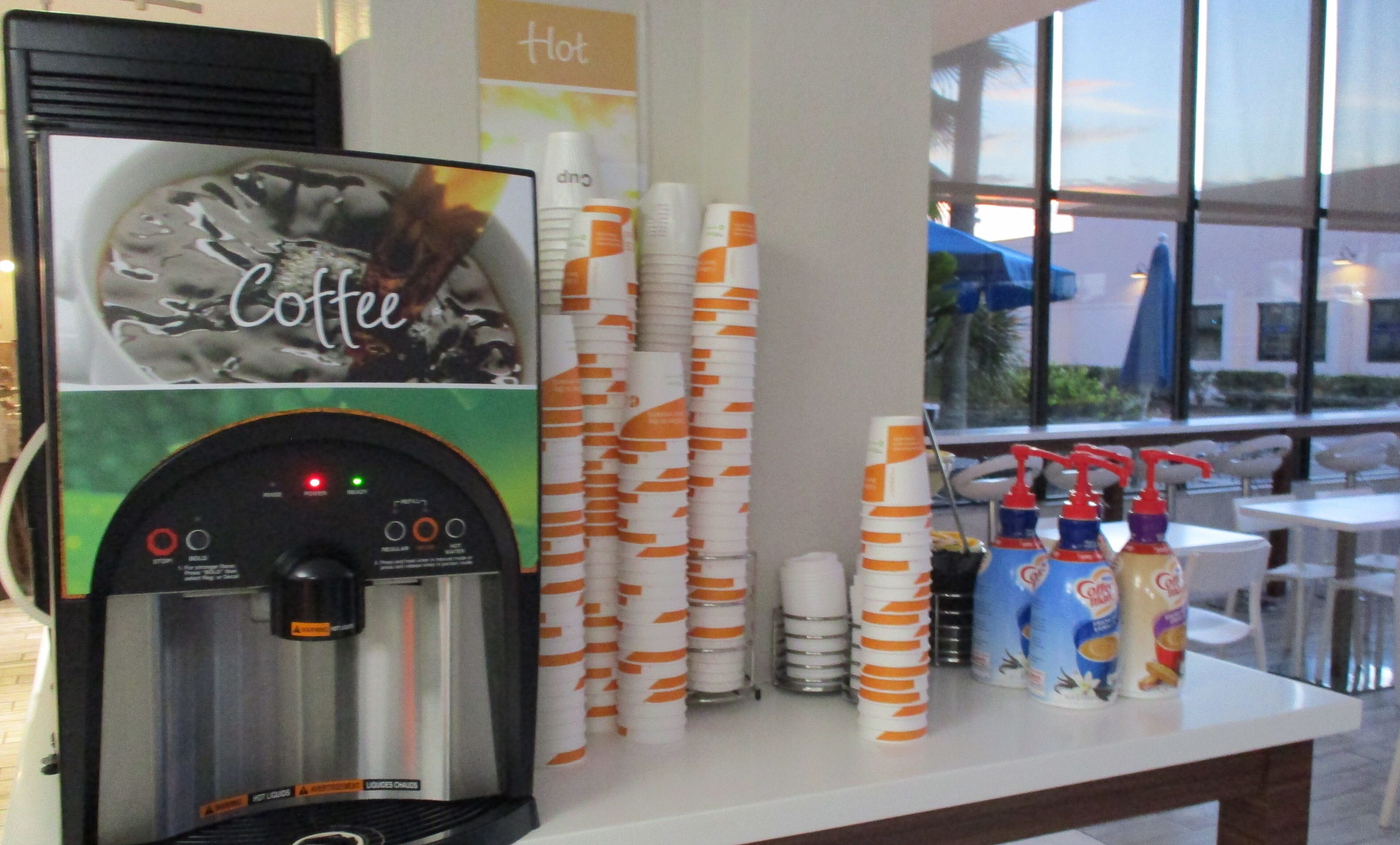A coffee machine and disposable cups on a counter with a window view.