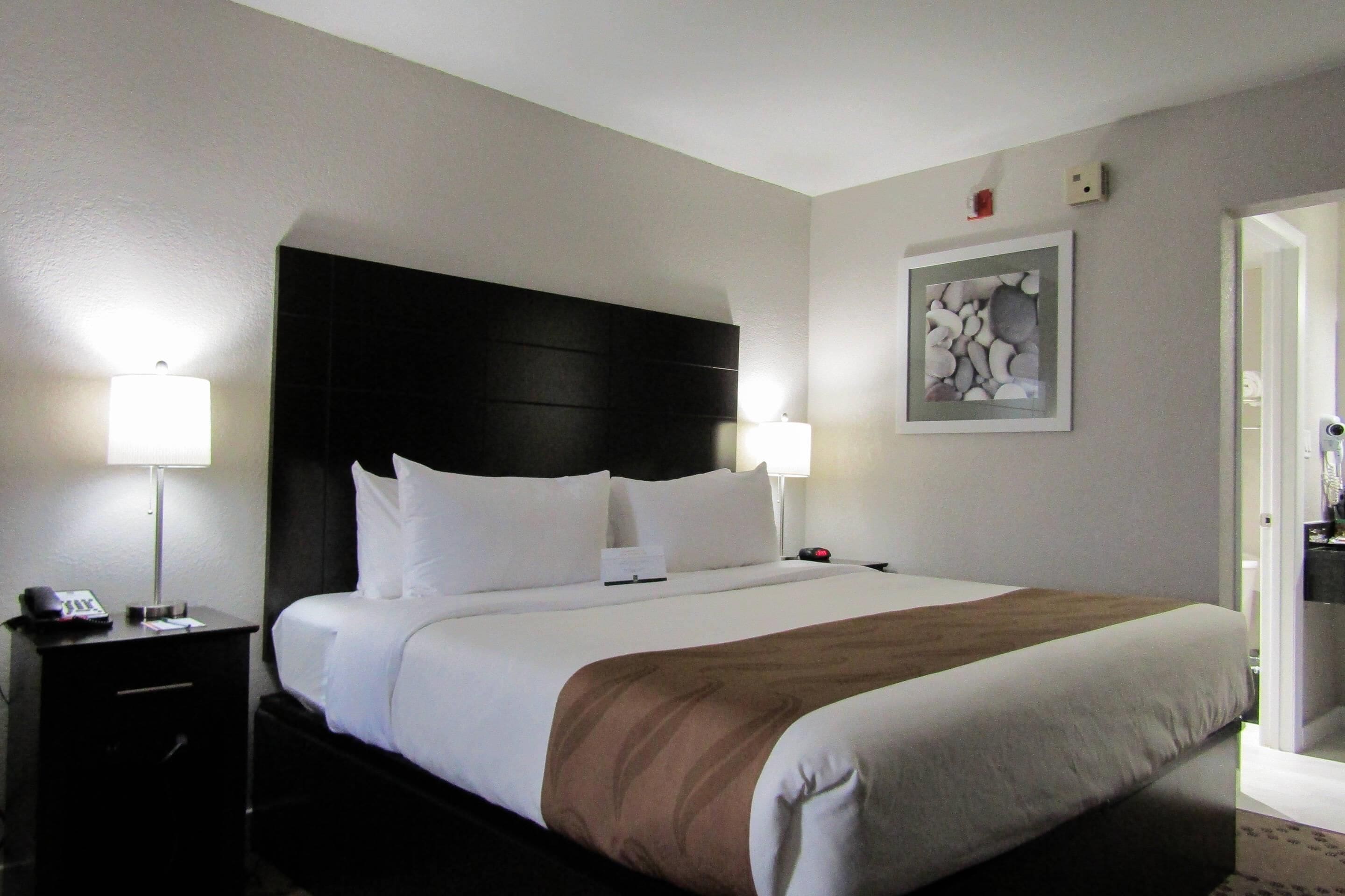 Quarto de hotel com uma cama grande, duas mesas de cabeceira com abajures, uma cabeceira e um quadro na parede.