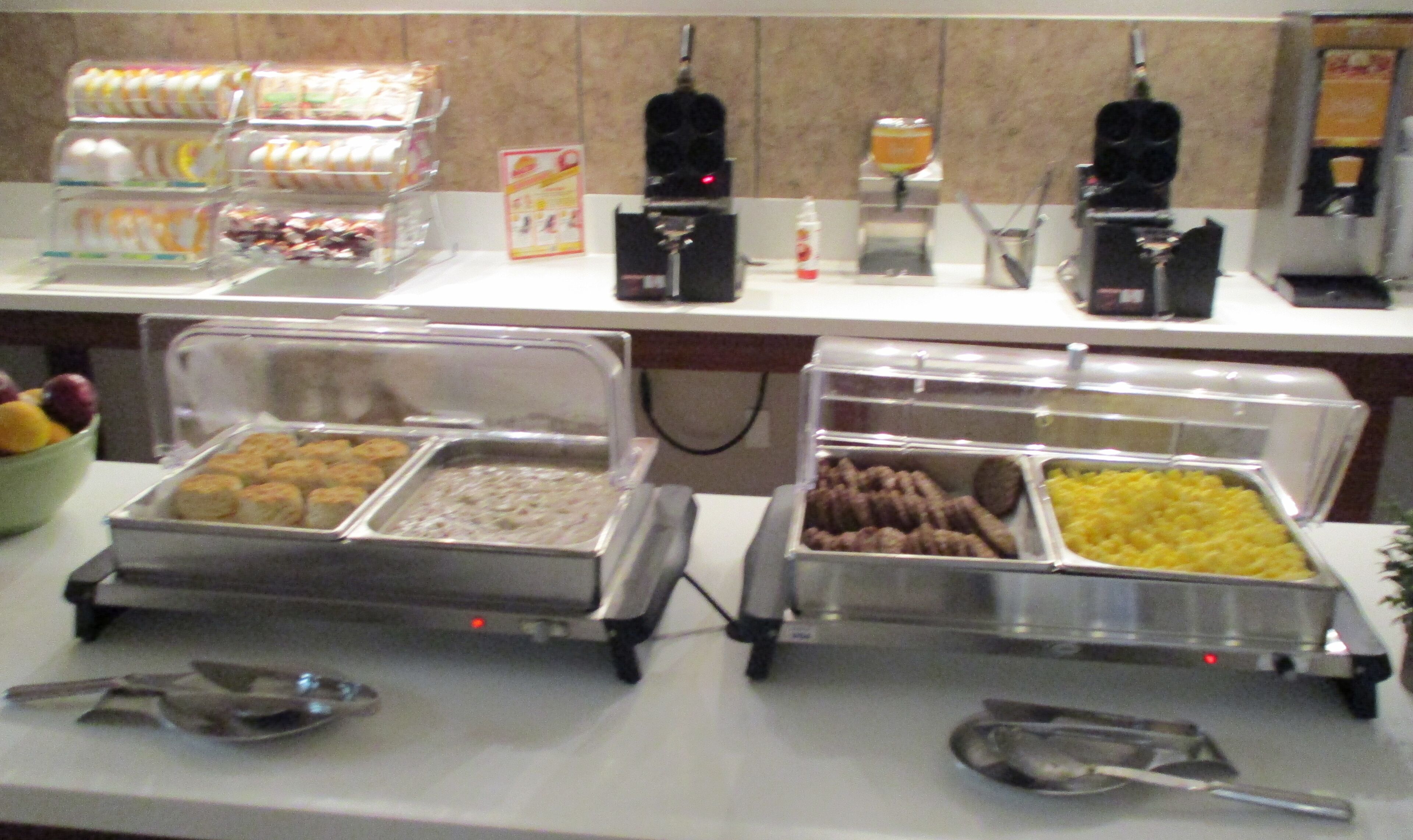 Un bufé con diversas opciones de comida en recipientes transparentes, como carnes, quesos y frutas.