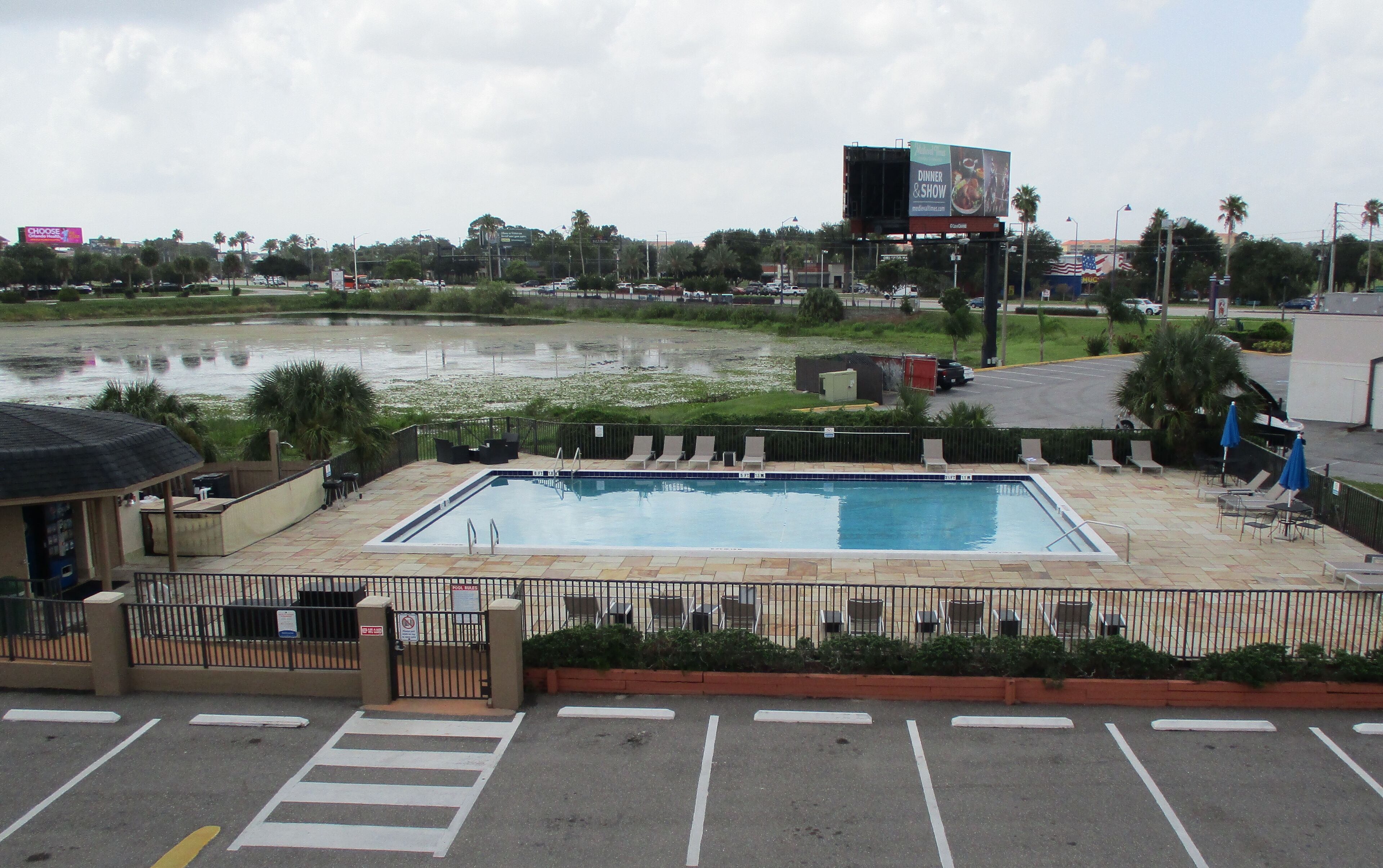 A swimming pool with a fenced area, lounge chairs, and a view of a body of water and distant buildings.