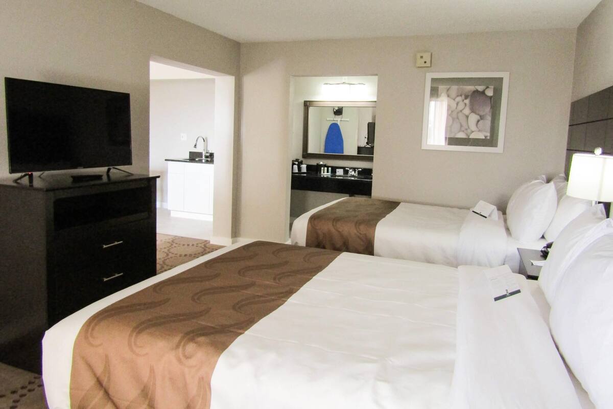 A hotel room with two beds, a TV, a desk, and a bathroom visible through an open door.