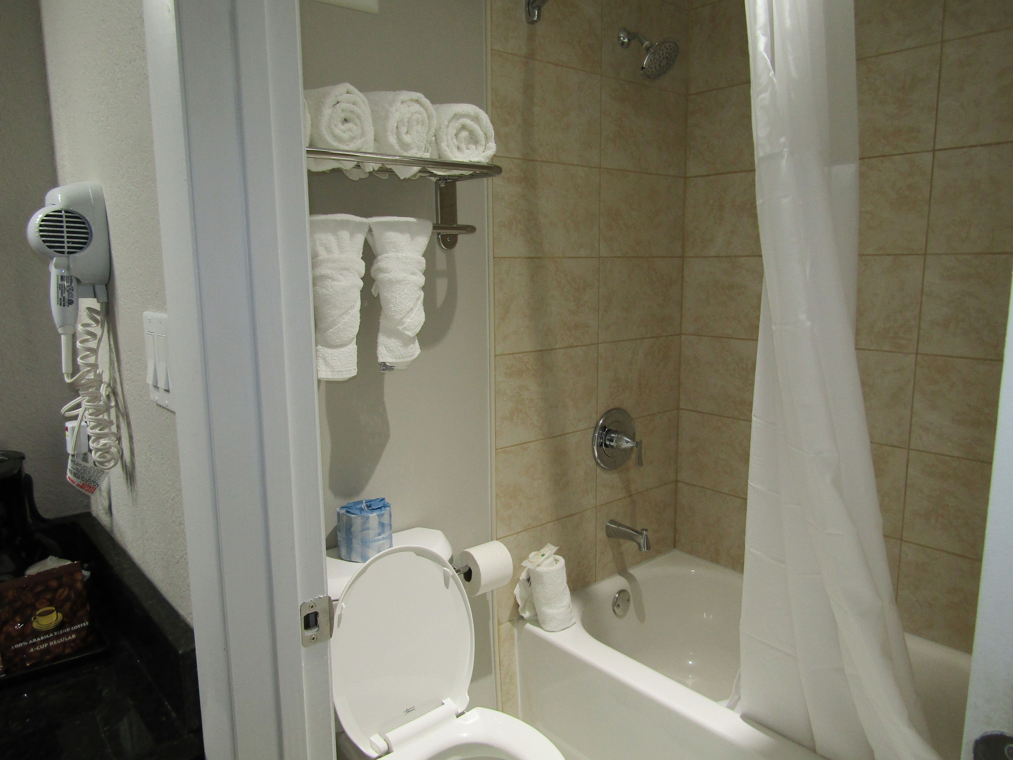 A bathroom with a toilet, a bathtub, and a shower. There are towels and a hairdryer on the wall.