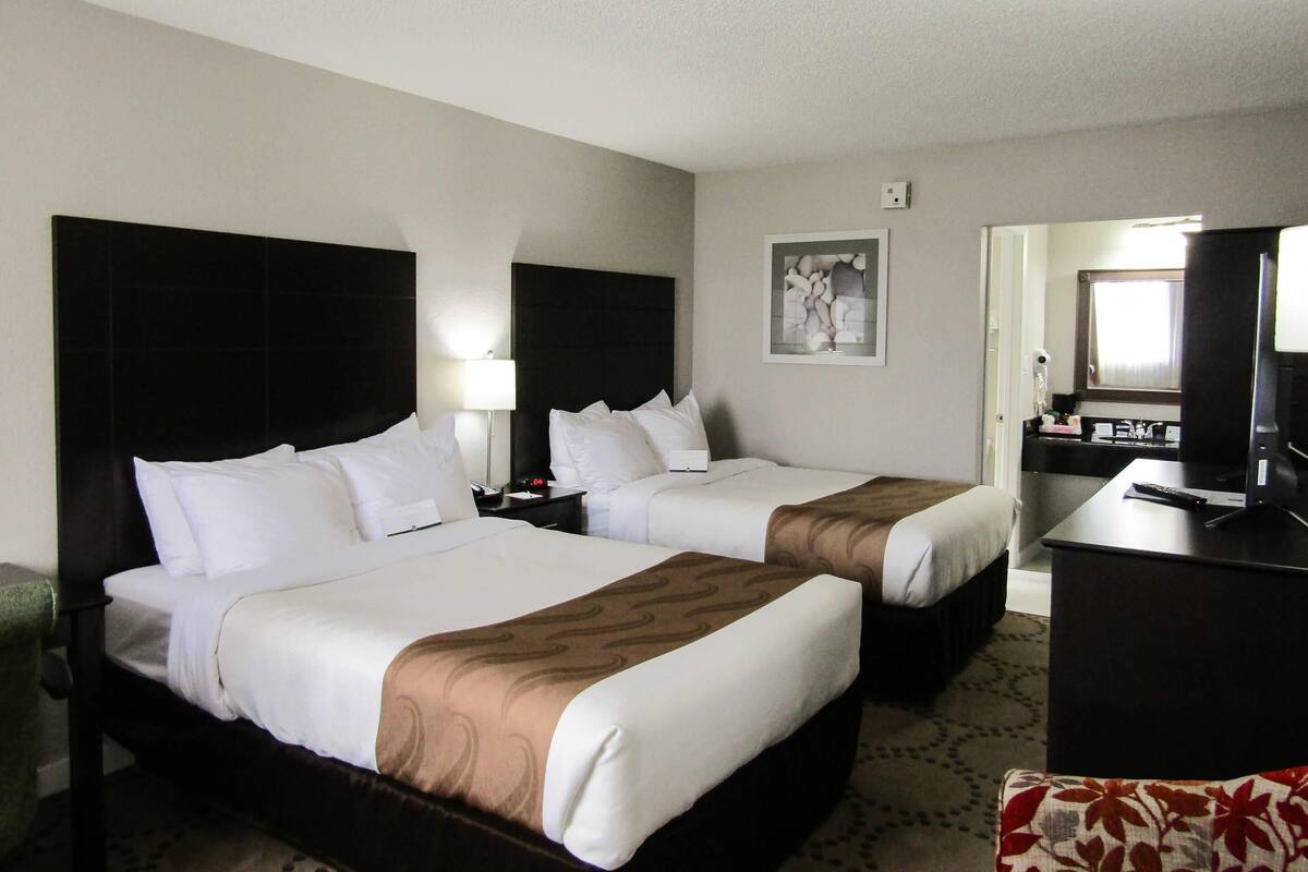 A hotel room with two beds, a desk, and a mirror.