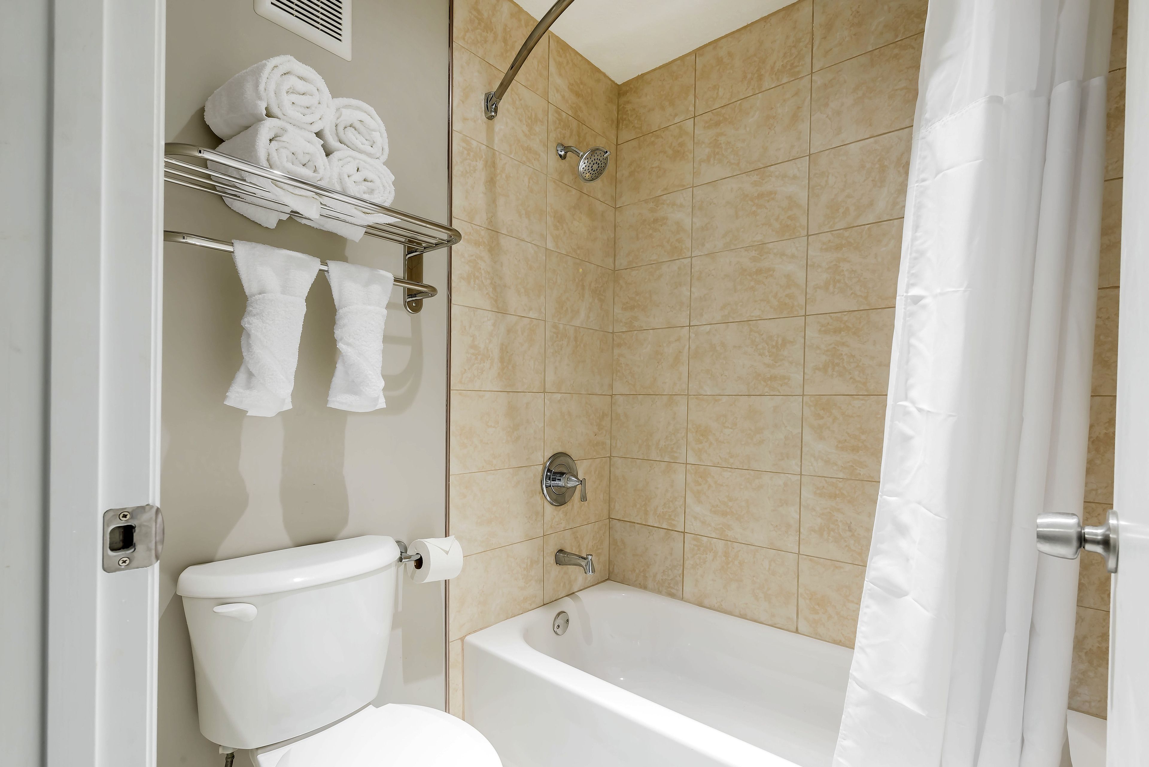 A bathroom with a toilet, a shower, and a bathtub. There are towels on a shelf above the toilet.