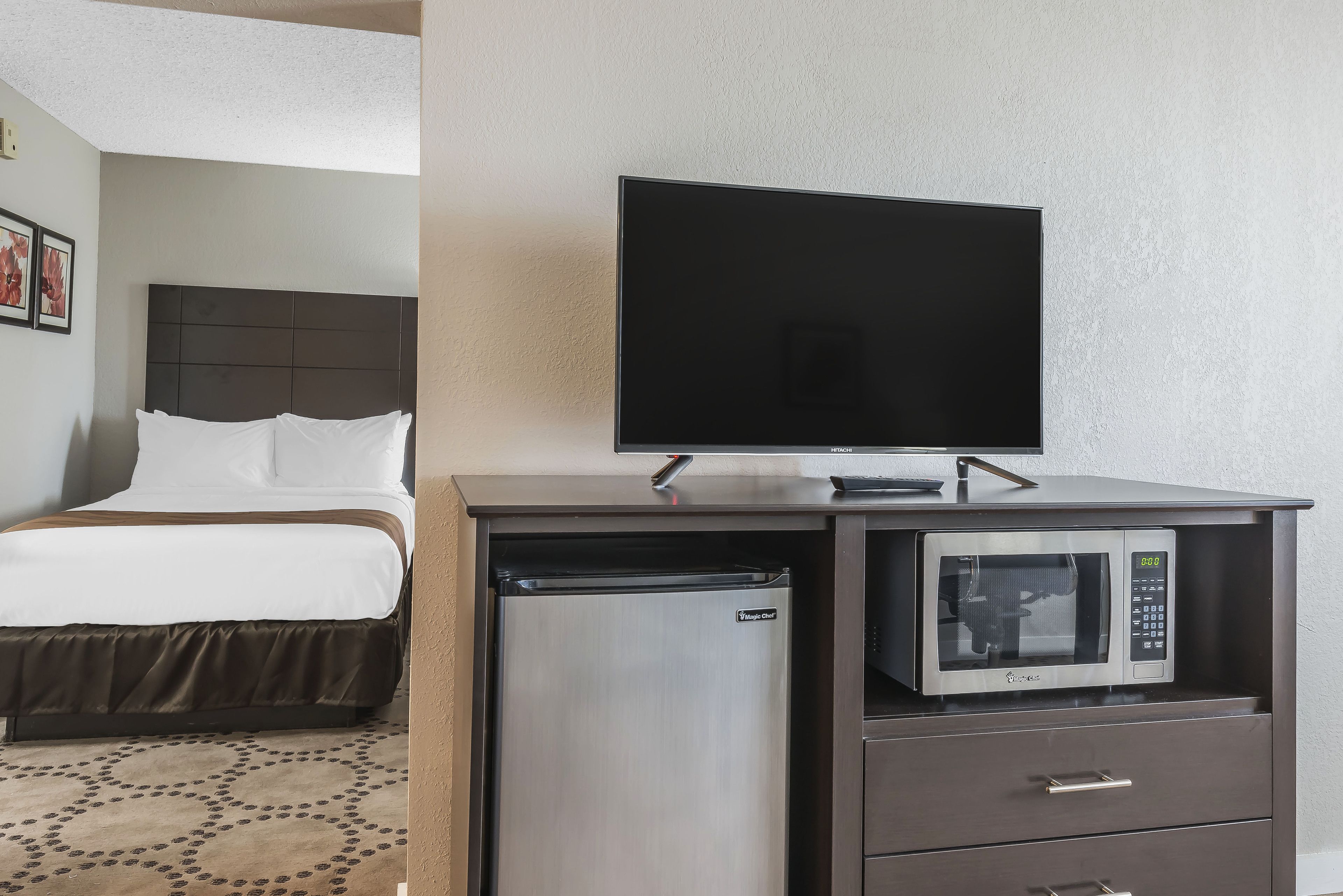 Habitación de hotel con cama, televisor de pantalla plana, refrigerador y microondas sobre un mueble de madera.