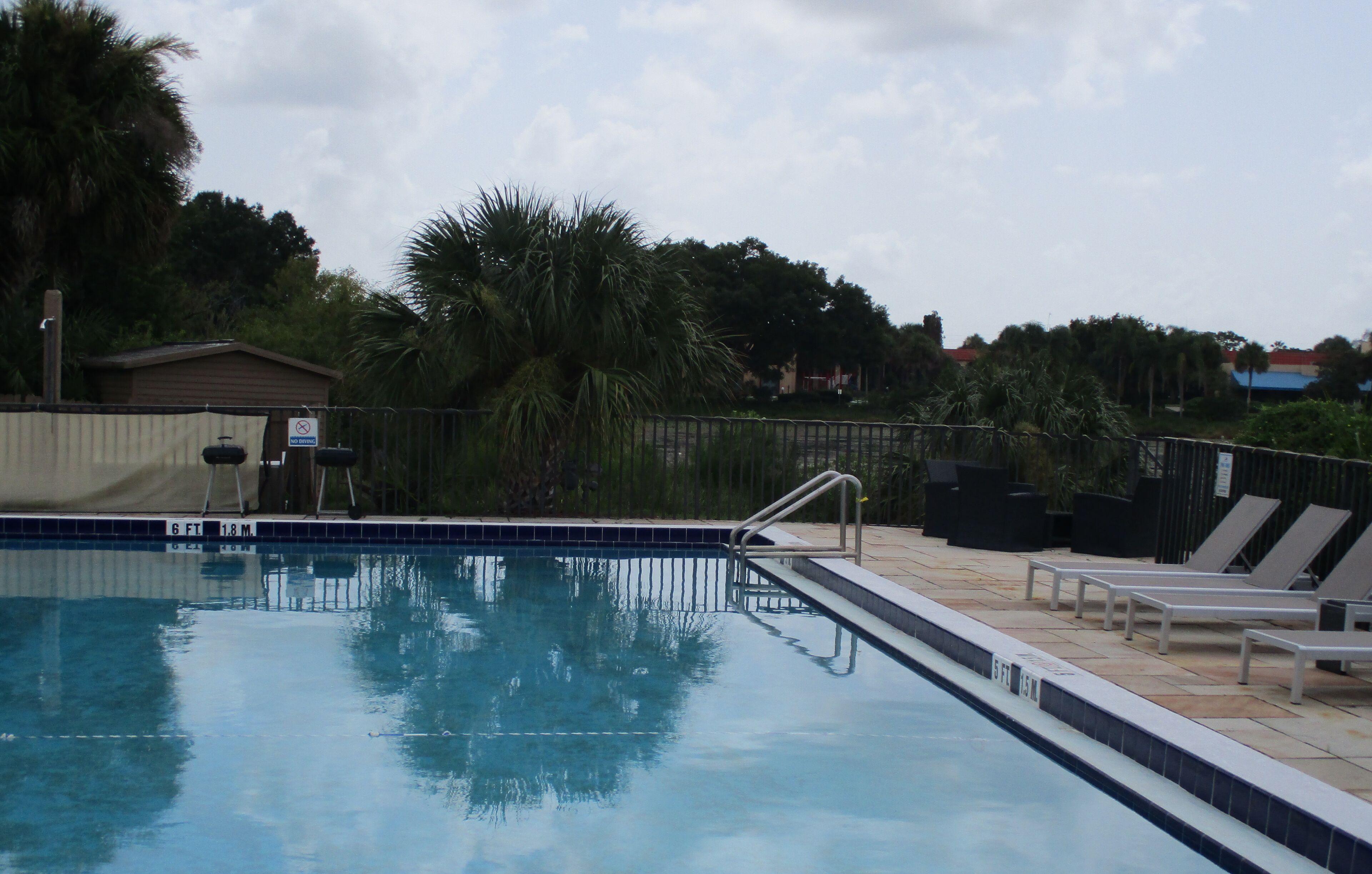 A swimming pool with a tiled edge, a metal handrail, and lounge chairs.