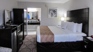 Habitación de hotel con una cama, un escritorio, un televisor, un espejo y un baño visible a través de una puerta abierta.
